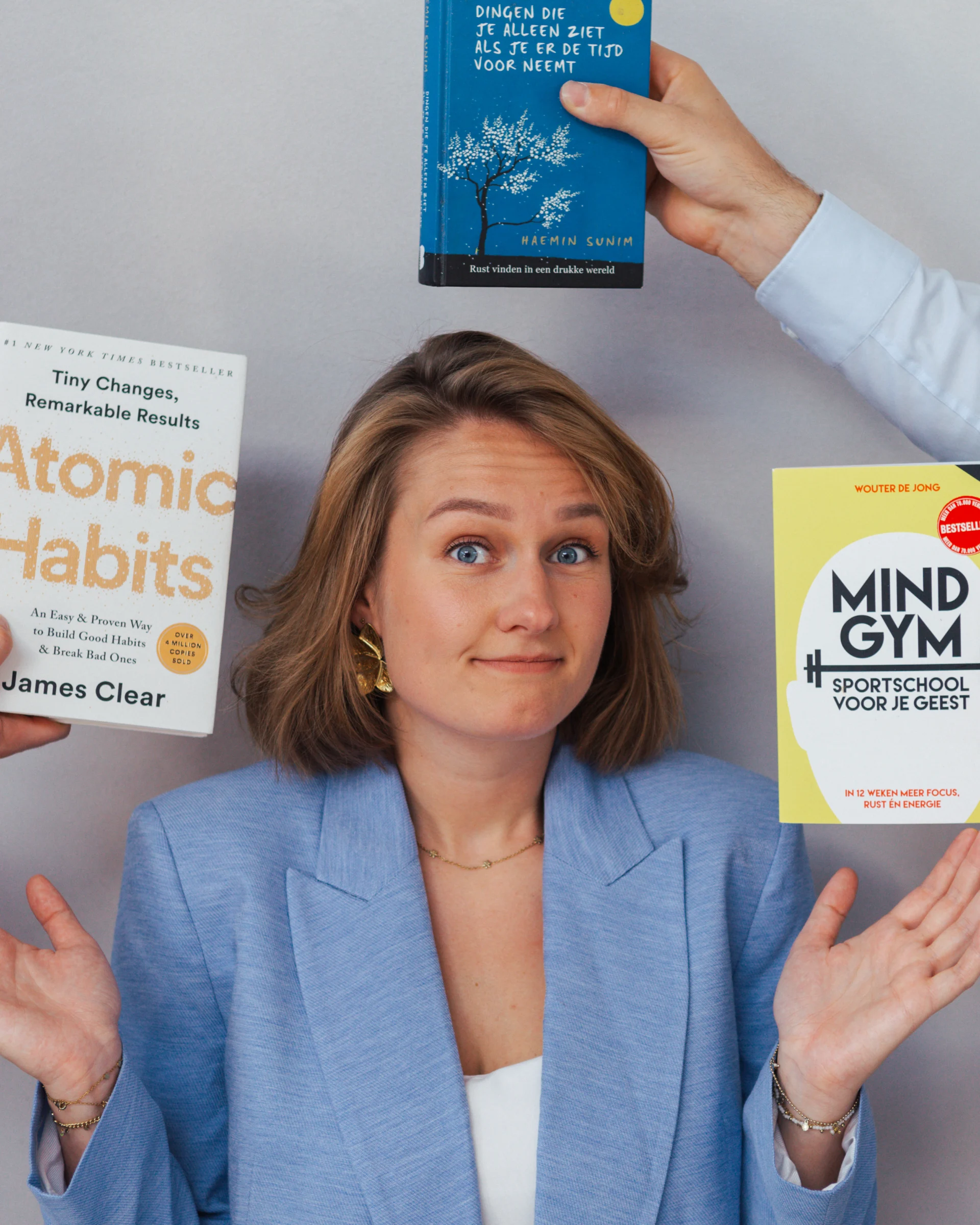 Sophie net mindset boeken Sophie in een lichtblauw jasje kijkt met een twijfelende blik omhoog terwijl drie verschillende zelfhulp- en mindsetboeken om haar heen worden vastgehouden: Atomic Habits, Mindgym en Dingen die je alleen ziet als je er de tijd voor neemt.